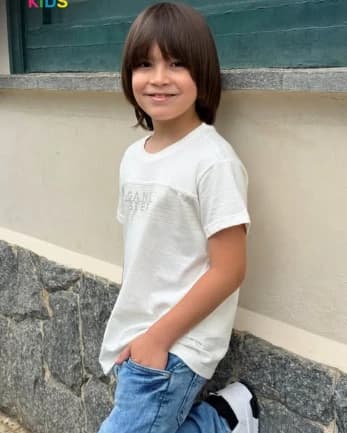 Criança com camiseta clara e calça jeans, em fotografia da Opinião Kids